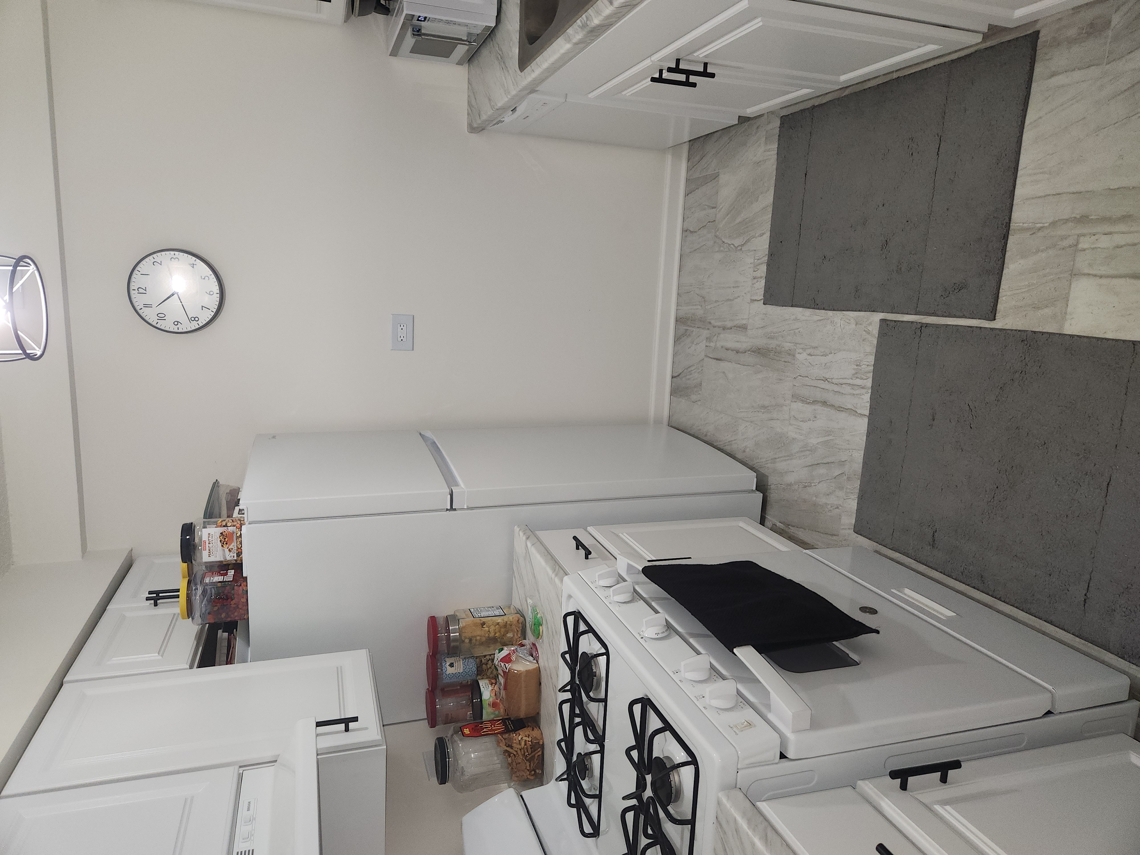 A white kitchen with a stove top oven and a clock on the wall.